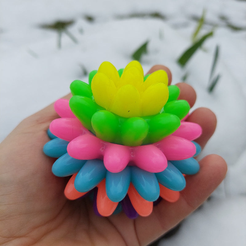 spiky regenbogen stuiterbal, massagebal, sensoriekbal, fidgetbal, motoriekspeelgoed, bal op hand met sneeuw op de achtergrond