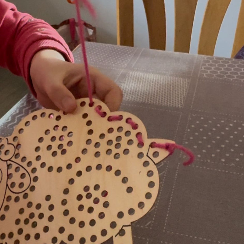 kinderhanden die een houten rijgschaap versieren met roze wol, fijn motoriek knutsel werk, motoriekspeelgoed